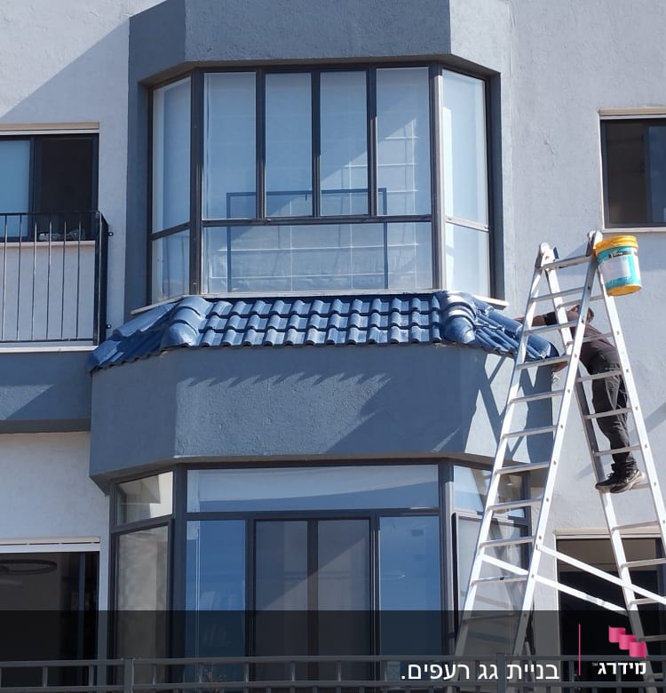 אדם על סולם צובע גג רעפים כחול